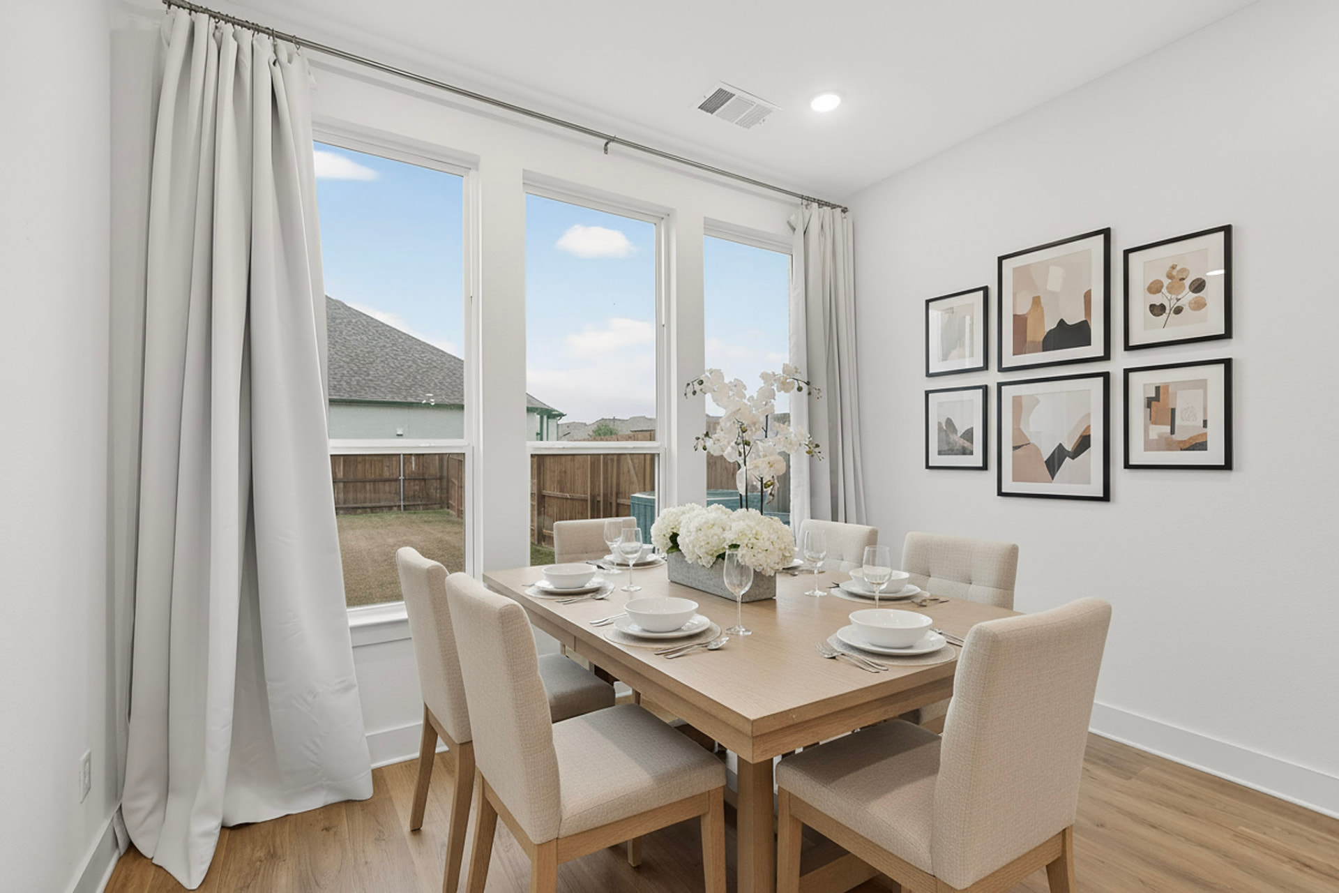 Dining area with a table and chairs, a gallery wall of framed art, full-length curtains and a window to the backyard.