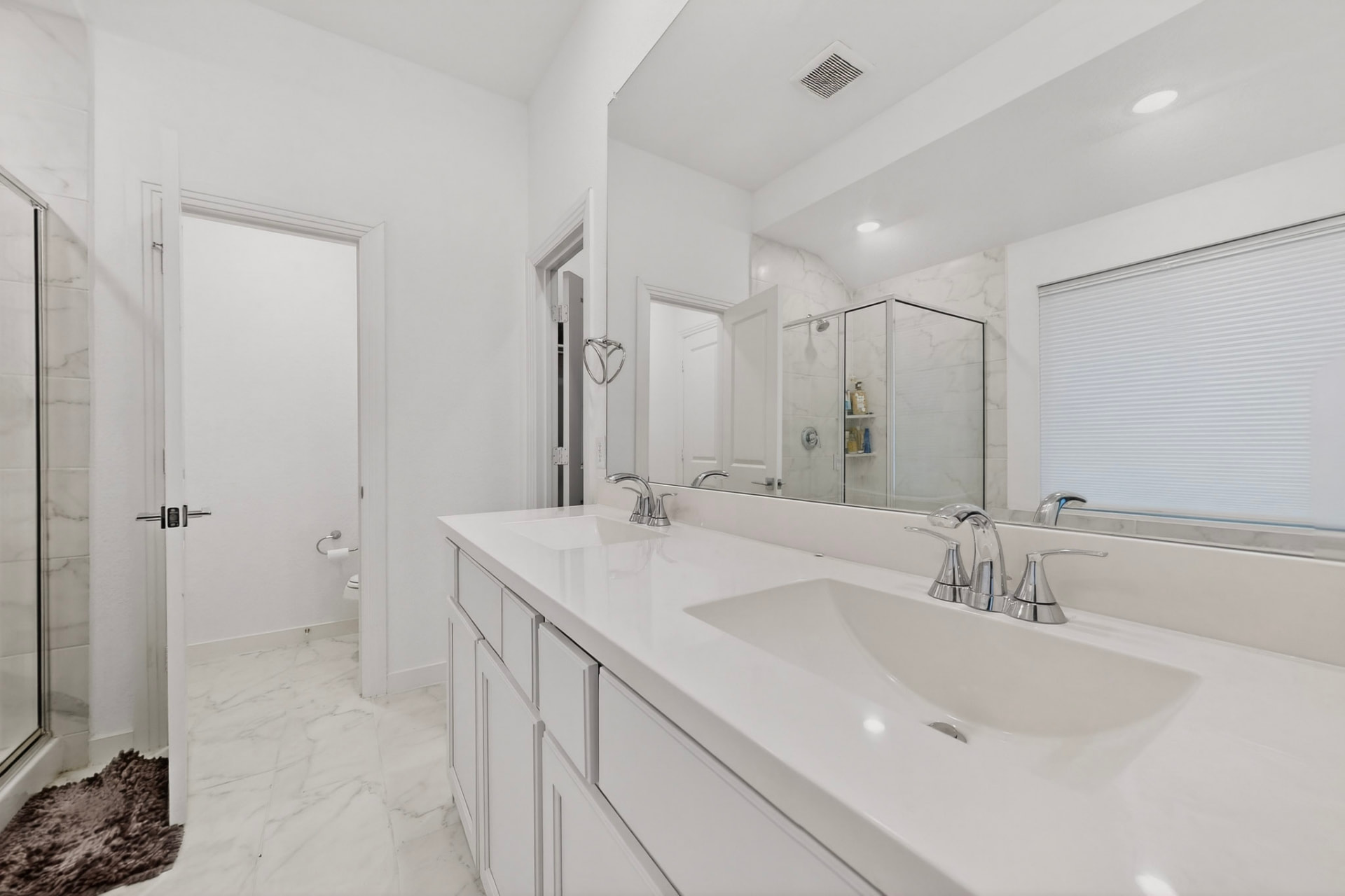 Primary bath vanity with a long white counter, two undermount sinks, chrome faucets, a full-width mirror and the water closet door at left.