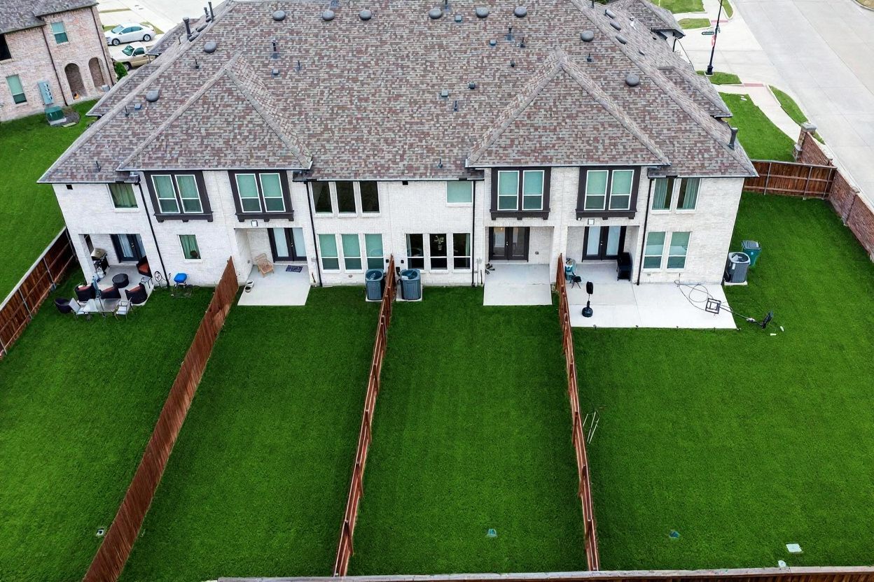 Aerial view looking down at the rear of the townhome row with green lawns and fenced yards.