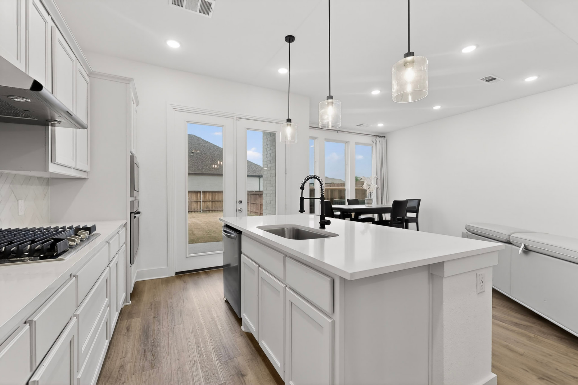 Kitchen with the five-burner gas cooktop and stainless vent hood, island with undermount sink and black spring-neck faucet, and the dining area and French doors beyond.