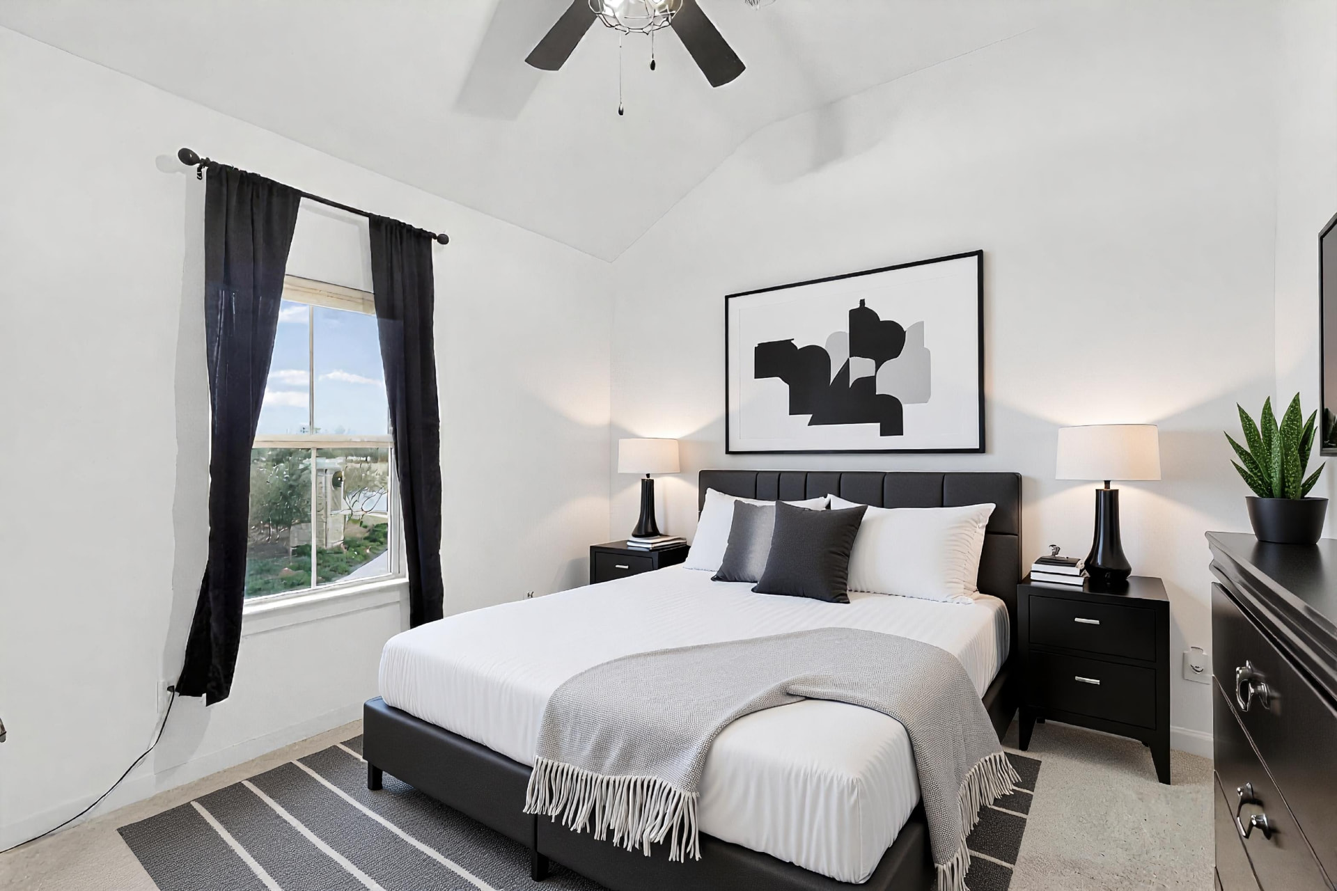 Secondary bedroom with grey bedding, a potted plant and a window with black curtains.