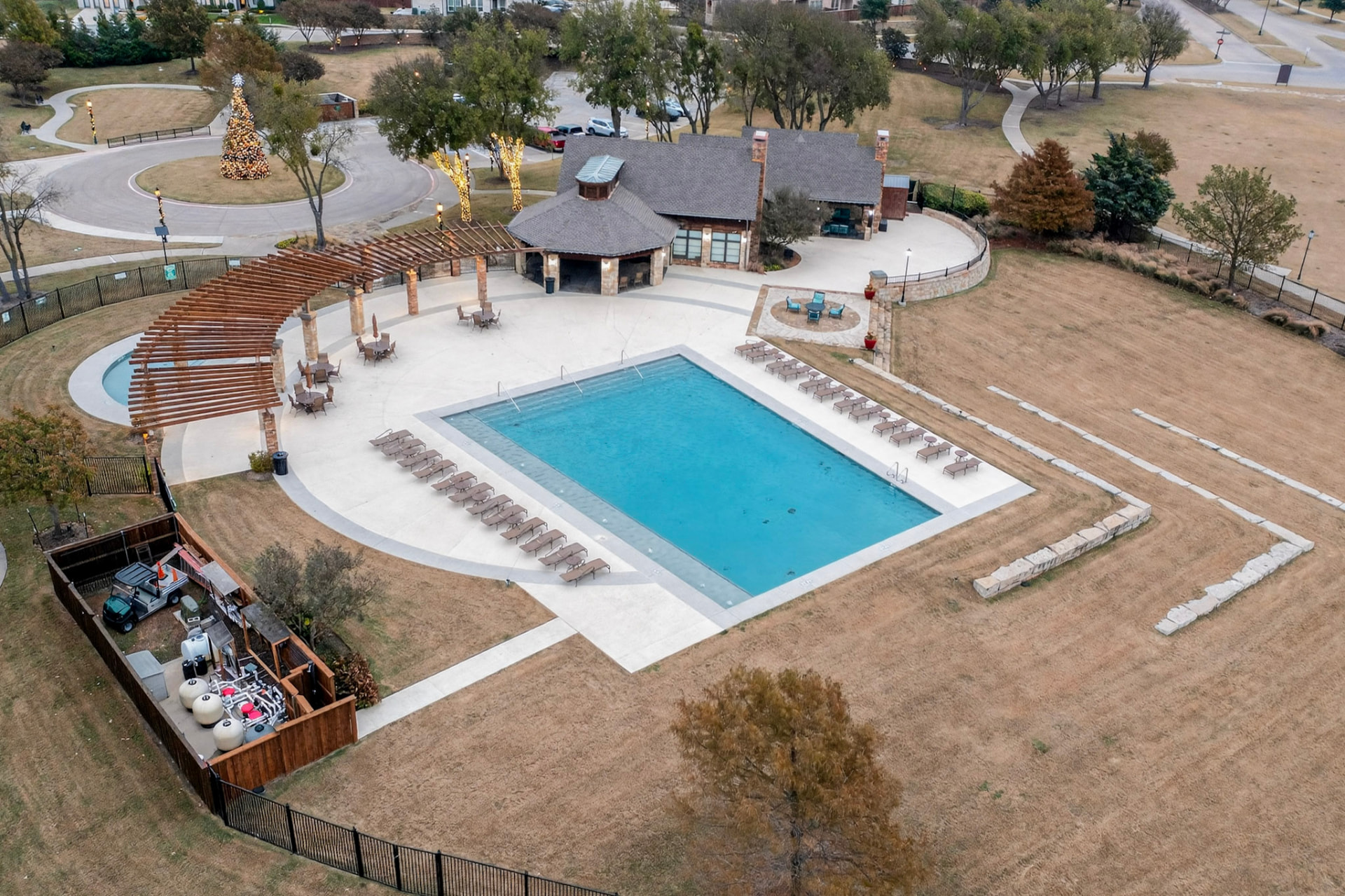 Aerial view of the Devonshire community pool and stone clubhouse with rows of loungers and a pergola.