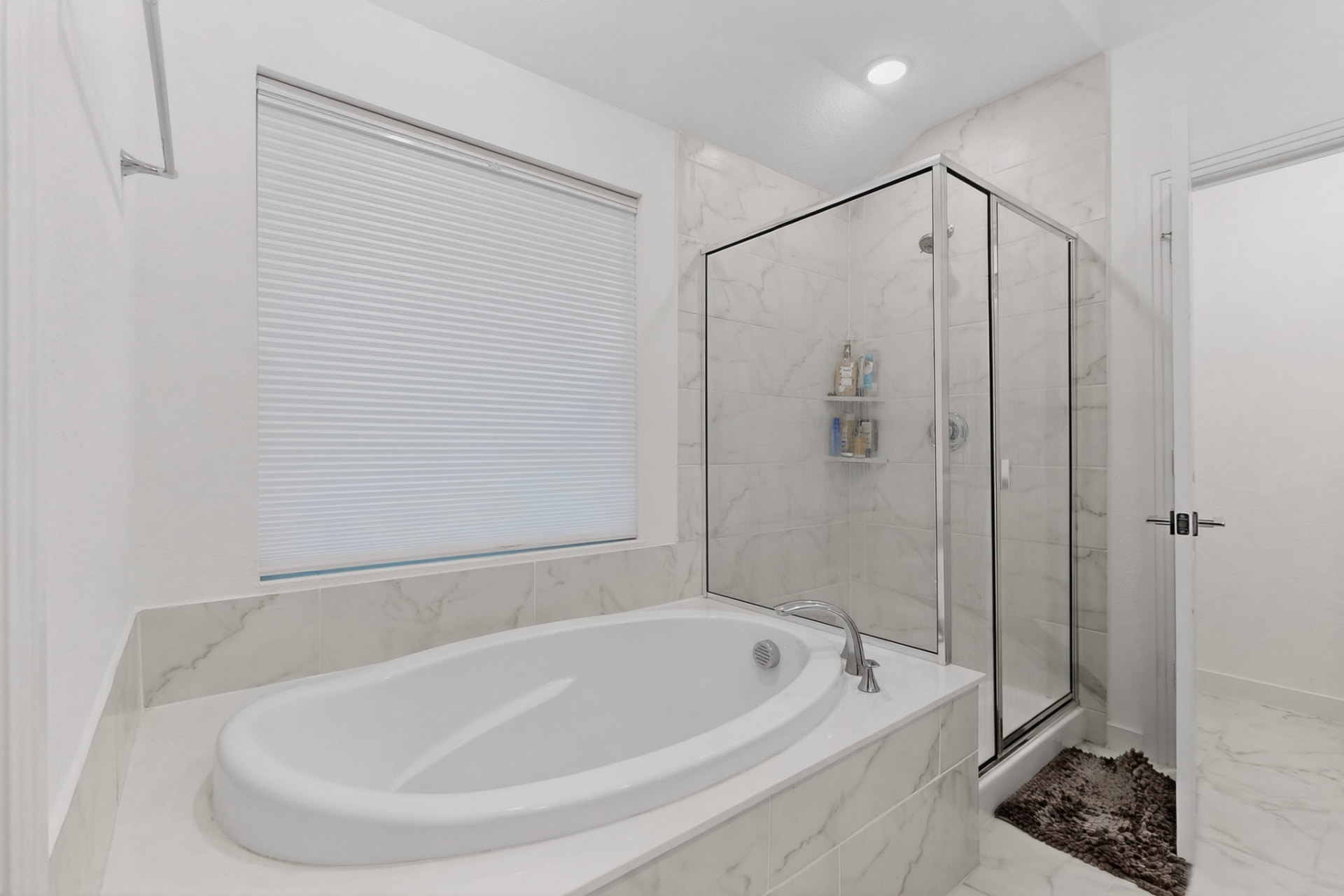 Primary bath with an oval garden tub beneath a window and a glass-enclosed corner shower in marble-look tile.