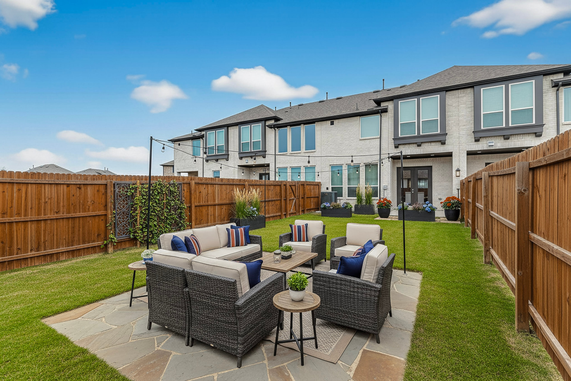 Fenced backyard with a grey patio sofa set with blue cushions and a side table on green grass.